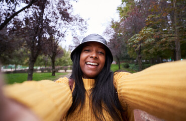 Happy African American woman taking a selfie outdoors in a park. Young latin lady looking at camera smiling making a photo for social media apps.