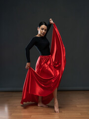 Dancer in a bright red skirt. Female dancer in a black bodysuit on a gray background.