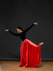 Dancer in a bright red skirt. Female dancer in a black bodysuit on a gray background.