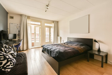 a bedroom with a bed, desk and television on the wall in front of the door to the balcony area