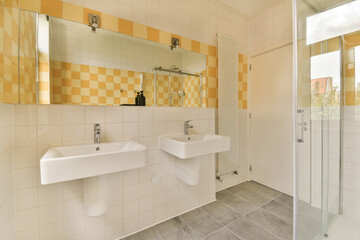 a bathroom with yellow and white tiles on the walls, two sinks and a shower stall in front of it