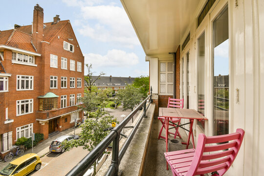 a balcony with two pink chairs and a yellow car parked on the sidewalk in front of the building is red