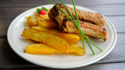 Just cooked portion of grilled pork ribs with pieces of fried potatoes served on table