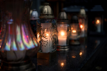 Decorative colored-glass grave candles glowing with warm candlelight on a tombstone at dusk —...