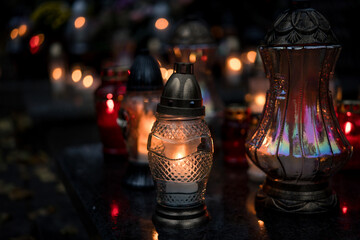 Decorative colored-glass grave candles glowing with warm candlelight on a tombstone at dusk —...