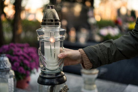 Hand placing a lit grave candle among flowers on a tombstone, close-up, Poland, November 1 — All Saints' Day (also known as All Souls' Day / Day of the Dead)