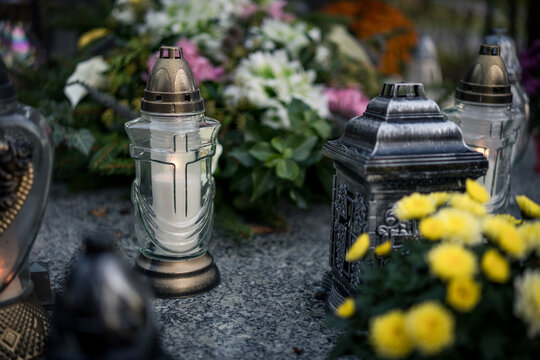 Lit grave candles among flowers on a grave at dusk &mdash; Poland, November 1, All Saints&rsquo; Day (also known as All Souls&rsquo; Day / Day of the Dead) decorations on the graves at evening