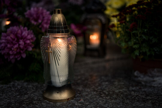 Lit grave candles among flowers on a grave at dusk &mdash; Poland, November 1, All Saints&rsquo; Day (also known as All Souls&rsquo; Day / Day of the Dead) decorations on the graves at evening