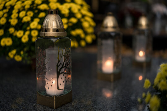Lit grave candles among flowers on a grave at dusk &mdash; Poland, November 1, All Saints&rsquo; Day (also known as All Souls&rsquo; Day / Day of the Dead) decorations on the graves at evening