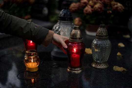 Hand placing a lit grave candle among flowers on a tombstone, close-up, Poland, November 1 &mdash; All Saints' Day (also known as All Souls' Day / Day of the Dead)