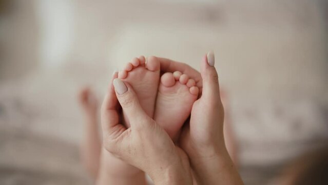 Mom gently tickling baby's tiny feet one finger, hands close-up. Congenital reflex finger flexion in infants, healthy body reaction. Mother enjoying motherhood checks baby health. Feet heart shape.