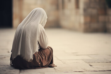 A rear view of a Muslim woman sitting on the ground in the street. Prayer for peace - obrazy, fototapety, plakaty