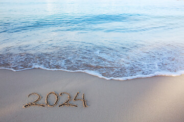 New Year 2024 handwritten in the white sand surface.