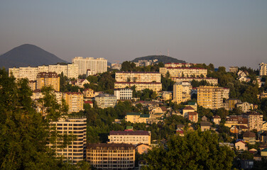 Fototapeta na wymiar Sochi, Krasnodar Krai, Russia - August, 7, 2023: panoramic view of residential buildings among green hills in the city center at sunset and space for copying