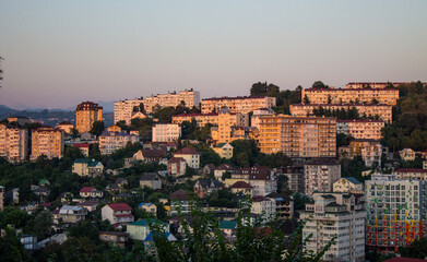 Fototapeta na wymiar Sochi, Krasnodar Krai, Russia - August, 7, 2023: panoramic view of residential buildings among green hills in the city center at sunset and space for copying