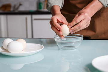 Female hands peeling off boiled egg shell on a kithcen table over glass plate.