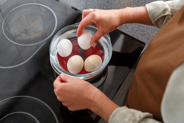 Hands putting eggs in a water in glass pot on  electric stove.