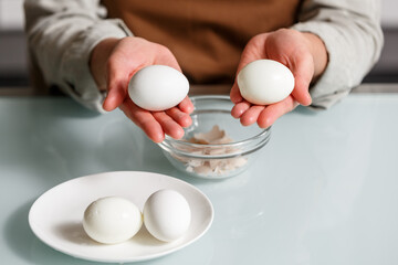 Female hands peeling off boiled egg shell on a kithcen table over glass plate. - 658789467