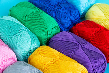 Background of multi-colored skeins of cotton yarn folded diagonally in a row. Materials for knitting. Textile industry. Arranged balls of yarn. Small depth of field.