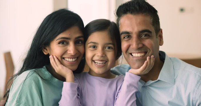 Close up portrait of cheerful loving Indian couple posing with child. Parents and little adorable daughter smile look at camera. Adoption, custody, upbringing, family love and ties, happy parenthood