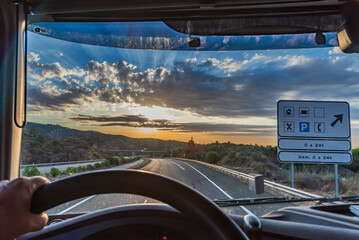View from the driving position of a truck of a highway with a 24-hour service area informative traffic sign. Dramatic sunset sky.