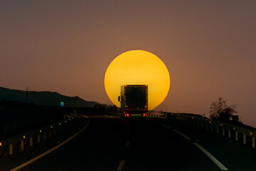 Silhouette against a sunset sun of a truck with a refrigerated trailer driving on the highway.
