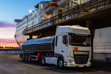 Fuel tank truck waiting next to a ferry to supply it. - obrazy, fototapety, plakaty