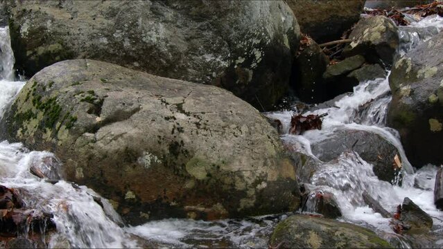 A close-up of a tranquil stream cutting through an array of large boulders and rocks. Coursing through a rugged landscape during the winter season.  4K footage.