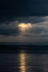 Sunset on Trasimeno lake in Umbria, Italy, with the sun coming down behind moody clouds and beautiful water reflections - 658801226