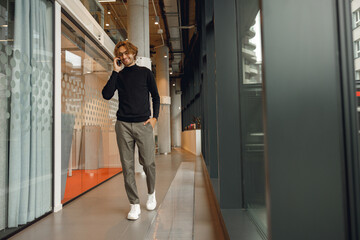 Handsome male freelancer in eyeglasses is talking phone standing in modern coworking space