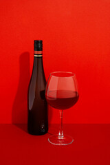 Bottle and glass of wine. Alcoholic drink on red background with deep shadows