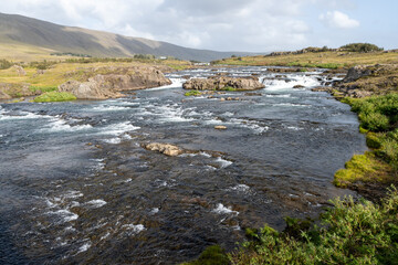 River with many picturesque cascades on Route 47 near Reykjavik, Iceland under sunny autumn cloudscape.