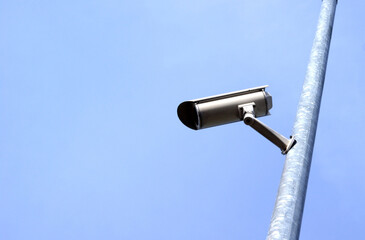 Surveillance analog camera on a pole against a blue sky