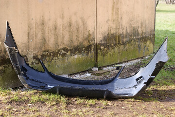 A plastic damaged bumper of a passenger car discarded next to a garbage can