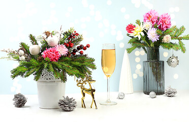 Christmas creative bouquet of live fir branches in a vase, with chrysanthemum flowers, decorations and a glass of champagne on an elegant festive background. Christmas and New Year mockup for design