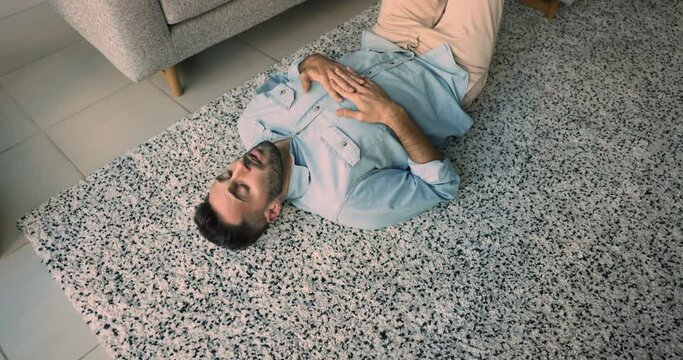 Above view of young upset Hispanic guy lying on carpet in cozy living room, feeling uncertain, thinking about unpleasant life situation, looking lonely, lazy or unmotivated spend time alone at home