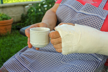 old woman with a cup of coffee in her hands, one of them with a cast
