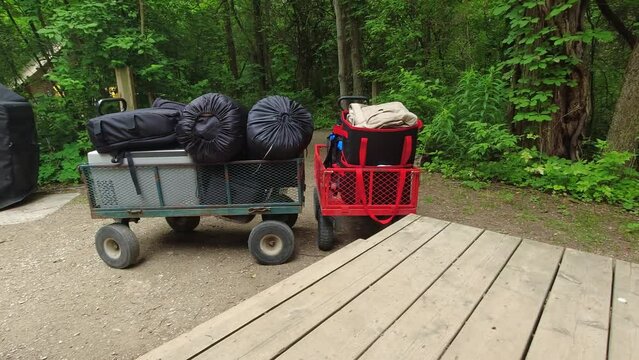 Camping cart on wheels at near camp cabin. Camping wagon with gear and equipment at national park tour in the forest. Cart containing sleeping bags for tent, portable freezer and clothes outfit.