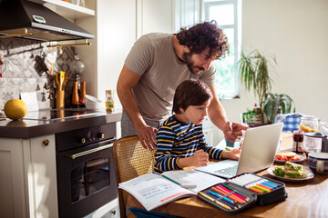 Young father helping his son with online class on a laptop at home