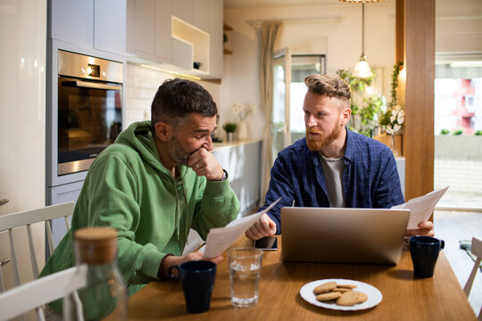 Concerned young gay couple going over bills and payments together at home