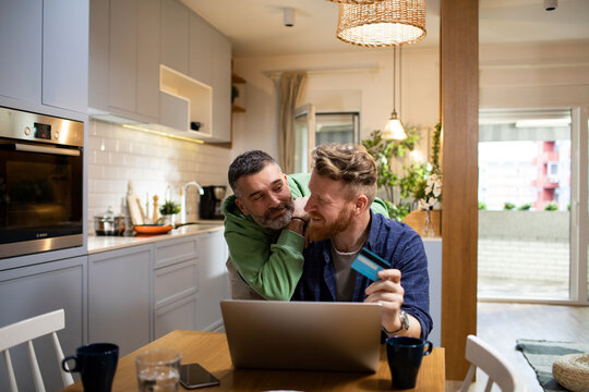 Young gay couple online shopping from a laptop at home