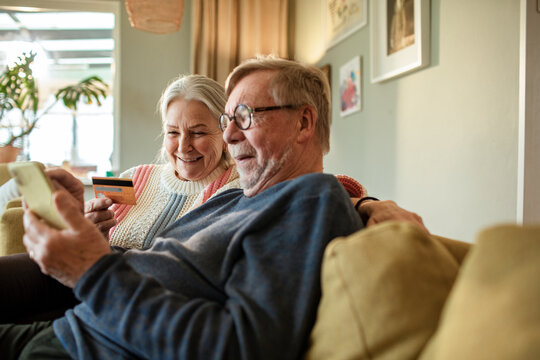 Senior Caucasian couple online shopping from a smartphone on the couch at home