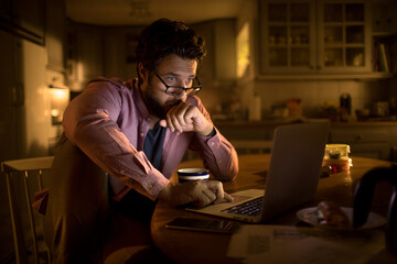 Stressed young man going over his bank balance on the laptop in the kitchen