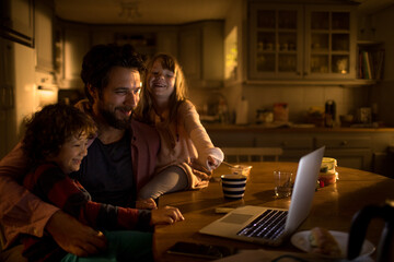 Young father using the laptop with his children for entrainment in the kitchen of their home