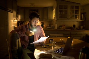 Young man reading his payments thoroughly at night in the kitchen