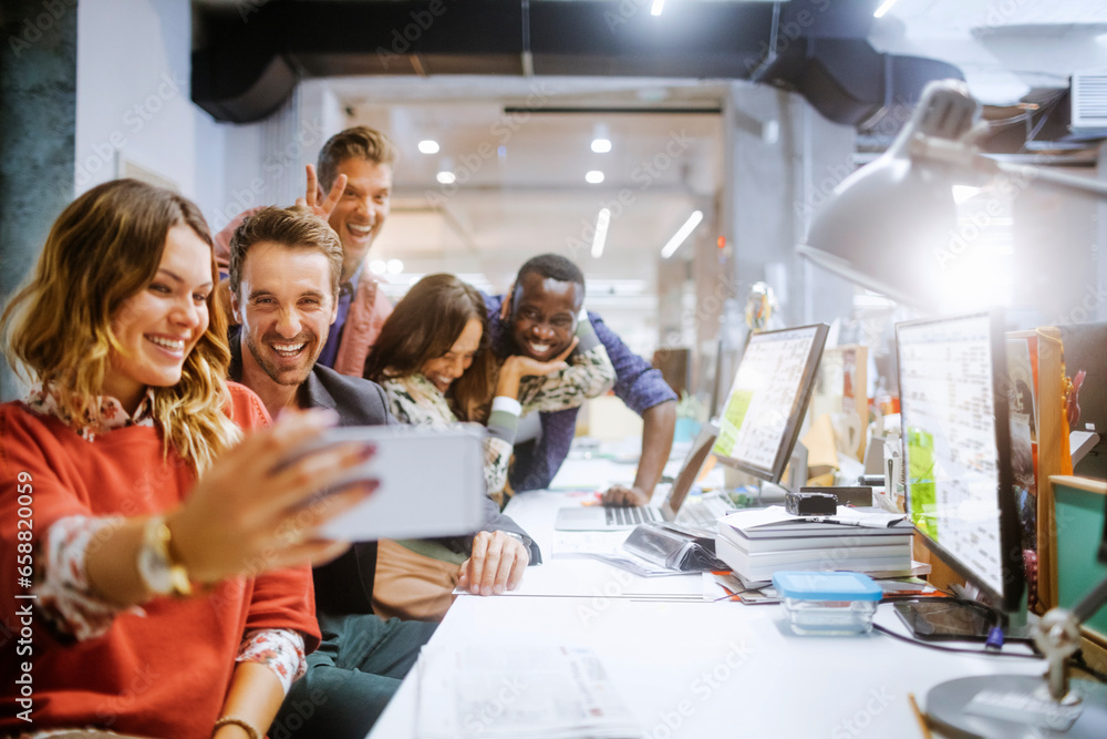 Wall mural Diverse group of coworkers taking a selfie on a smartphone in the office of a startup company