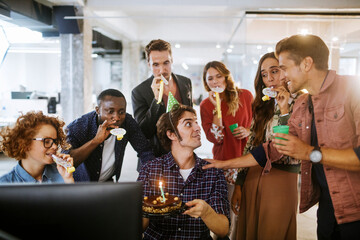 Young and diverse group of people celebrating a surprise birthday party in the office of a startup company