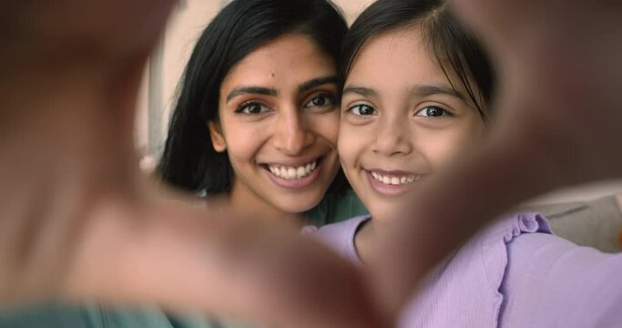 Close up portrait, beautiful faces of young Indian mom her adorable little 5s daughter making heart gesture, showing love sign to camera. I Love You, Happy Mothers Day celebration, family ties, bond