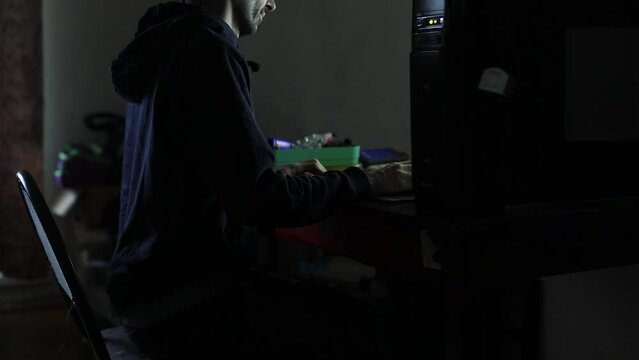 A guy is working at a computer in the dark. A student looking at the monitor. A man at his homework.