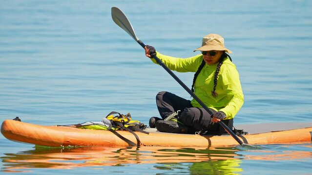 Lake Manitou, Manitoulin Island, woman sail on a SUP boards with special sport equipment, wet suit and life jacket for paddling. Stand up paddle boarding active recreation leisure and sport at lake.